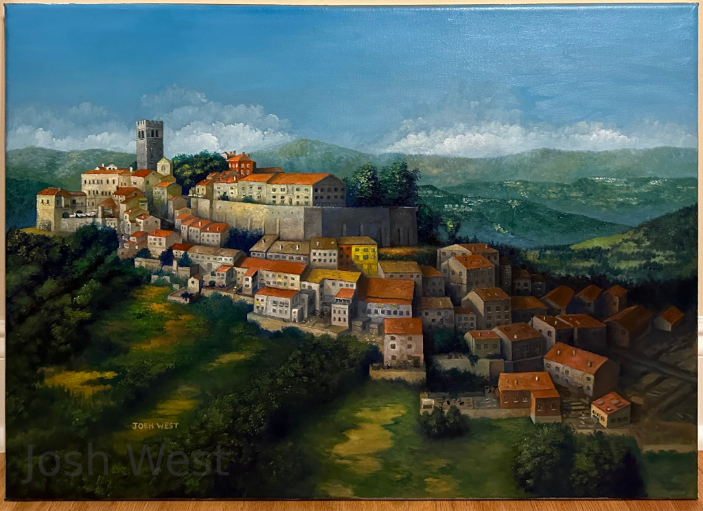 An aerial view of Motovun village in Croatia, which has a raised section with a tall tower looming over the rest of the village which sprawls out down the hillside.